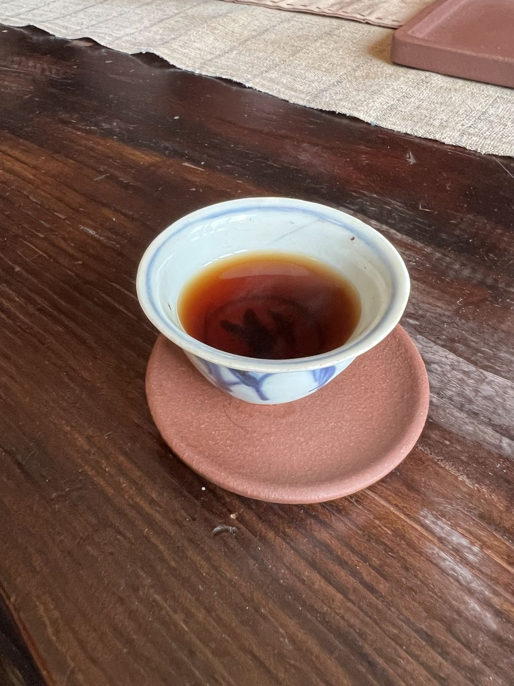 A small blue-and-white cup of dark tea on a clay saucer, on an old wooden table
